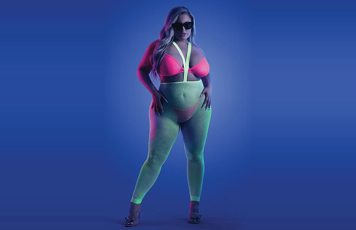 Model wearing a neon pink bralette and green suspender stockings under blue lighting